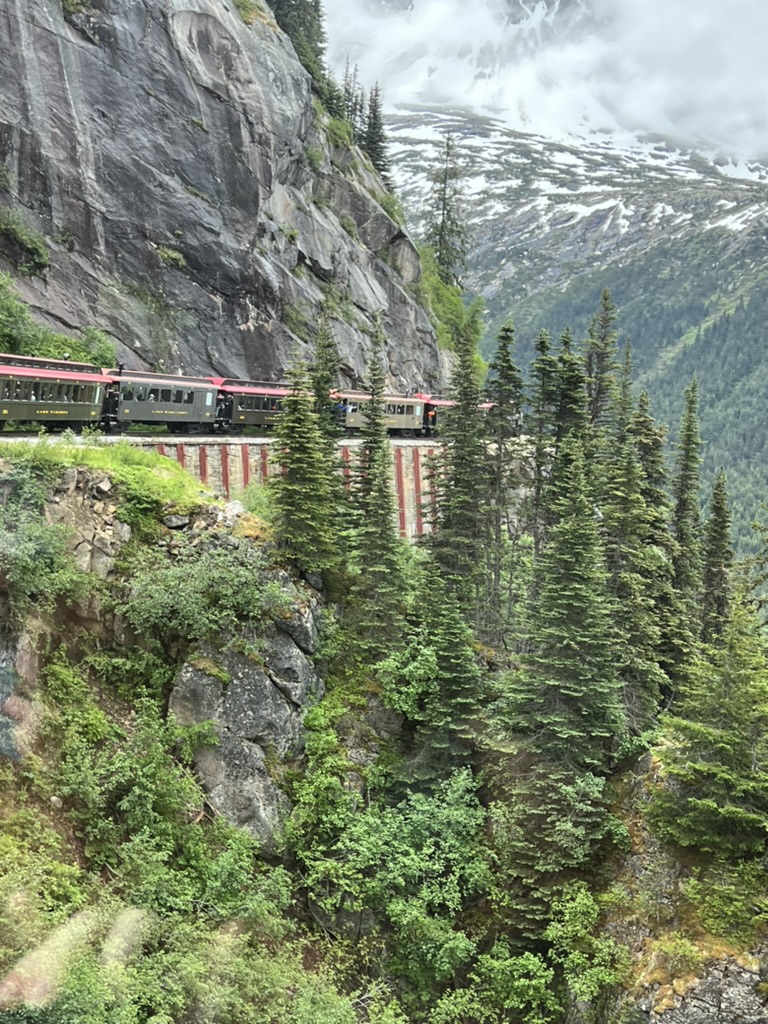 A vintage railway train on a mountainside trestle above forest in Skagway, Alaska